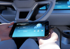 Person connecting a smartphone to a car's infotainment system, highlighting MD ELEKTRONIK's solutions for seamless in-vehicle connectivity and data integration.